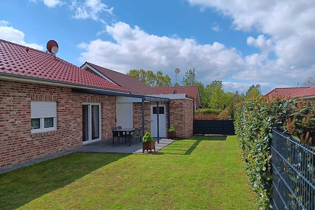 Garten des Ferienhauses mit Rasen, Hecke und Terrasse mit Tisch und Stühlen bei Sonnenschein