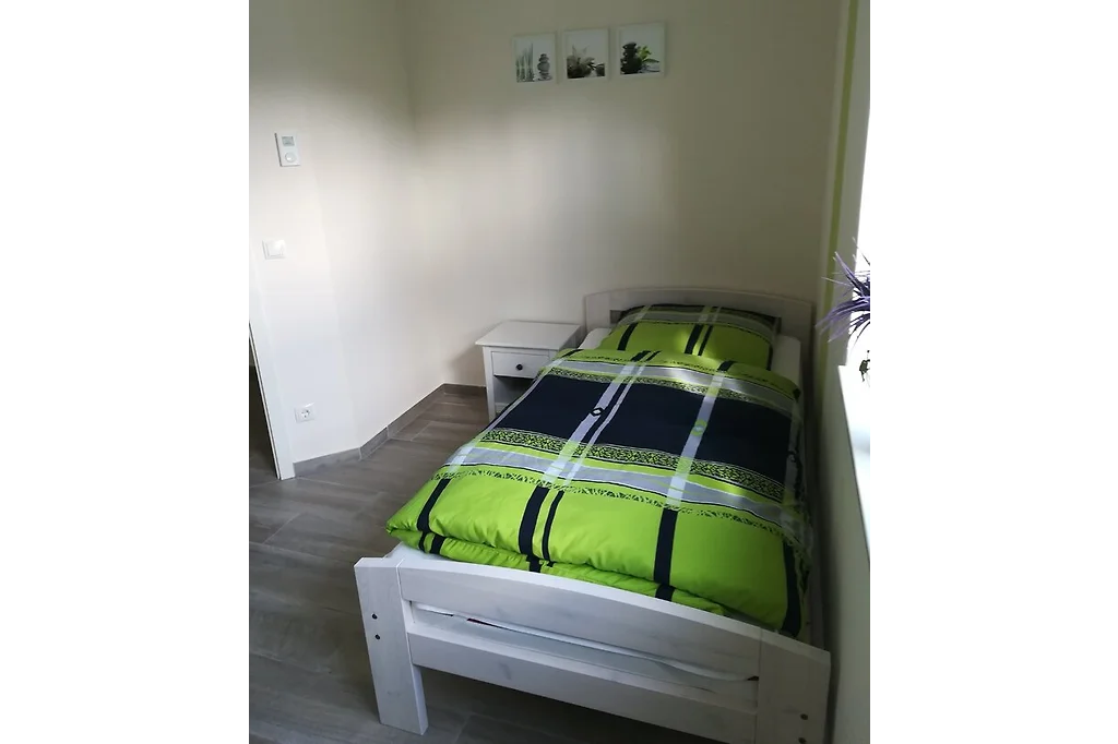 Schlafzimmer mit weißem Einzelbett, Nachttisch und Bildern an der Wand
