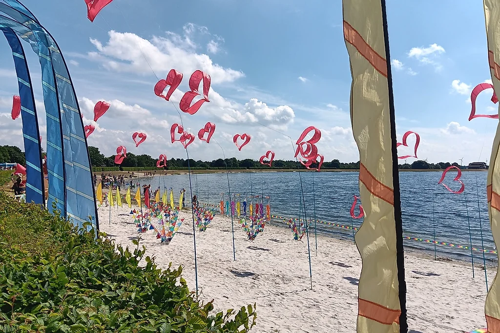 Bunte Fahnen und Windspiele am Sandstrand des Speichersees, dahinter das Wasser