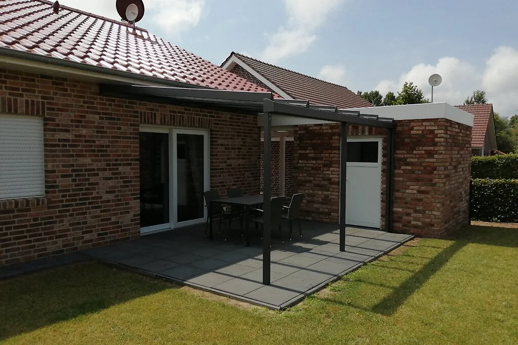 Terrasse mit Tisch und vier Stühlen vor der Schiebetür zum Wohnzimmer, davor Rasen